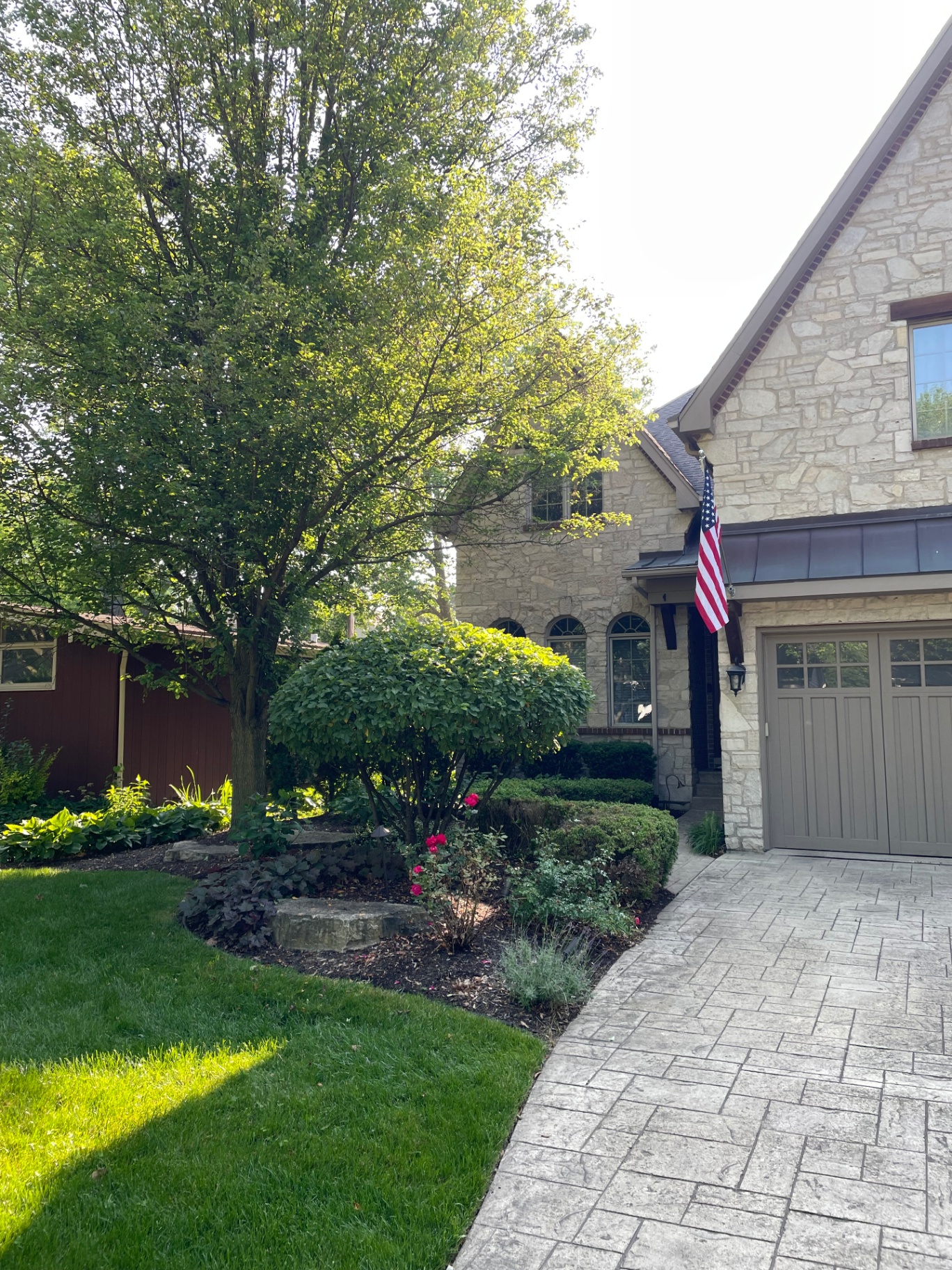 Stone cottage front yard with mature tree, manicured shrubs and stamped concrete walkway